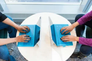 Dos personas trabajando en portátiles cara a cara, destacando el papel de la tecnología en el teambuilding digital